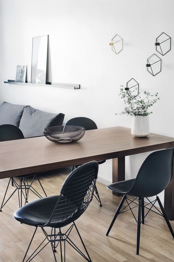a Scandinavian living and dining room with a grey sofa, a stained table, black Eames and Eames wire chairs and geometric sconces