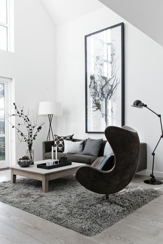 a Scandinavian living room with a graphite grey sofa and pillows, a black Egg chair, a low coffee table, an oversized artwork and a floor lamp