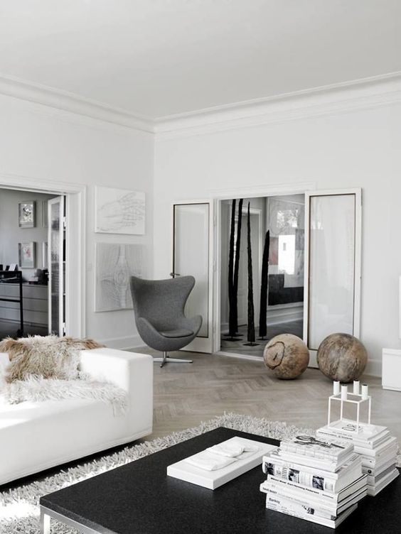 a Scandinavian living room with some large balls for decor, a white sofa with faux fur, a black coffee table and a grey Egg chair