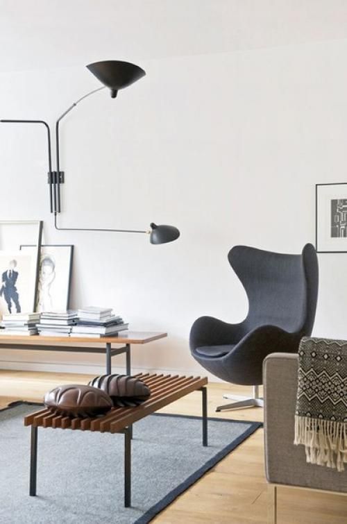 a Scandinavian living room with wooden benches, a black Egg chair, a grey sofa, a black sconce and some blankets