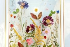 a beautiful and colorful pressed flower arrangement in purple, blue and mustard, with leaves is a super chic wall art