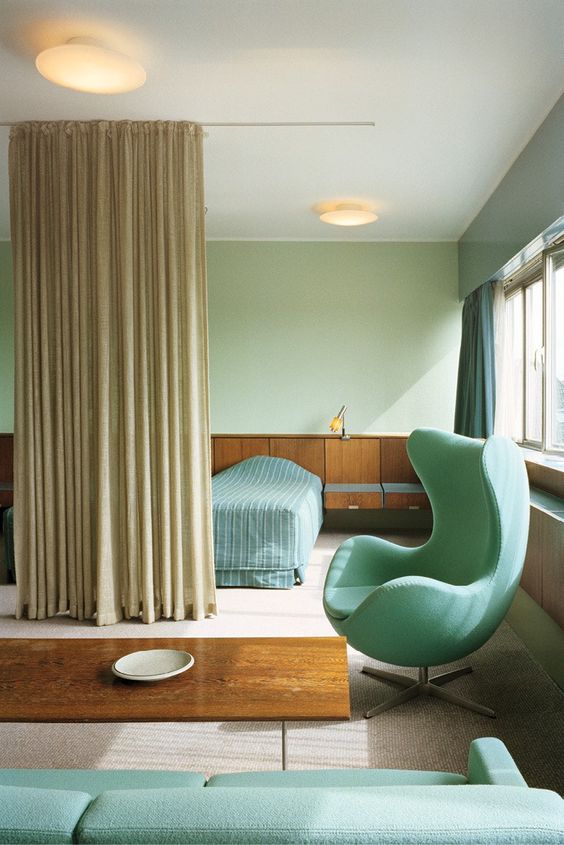 a beautiful space done in tan, light green and aqua, with a bed and floating nightstands, an aqua Egg chair and a sofa
