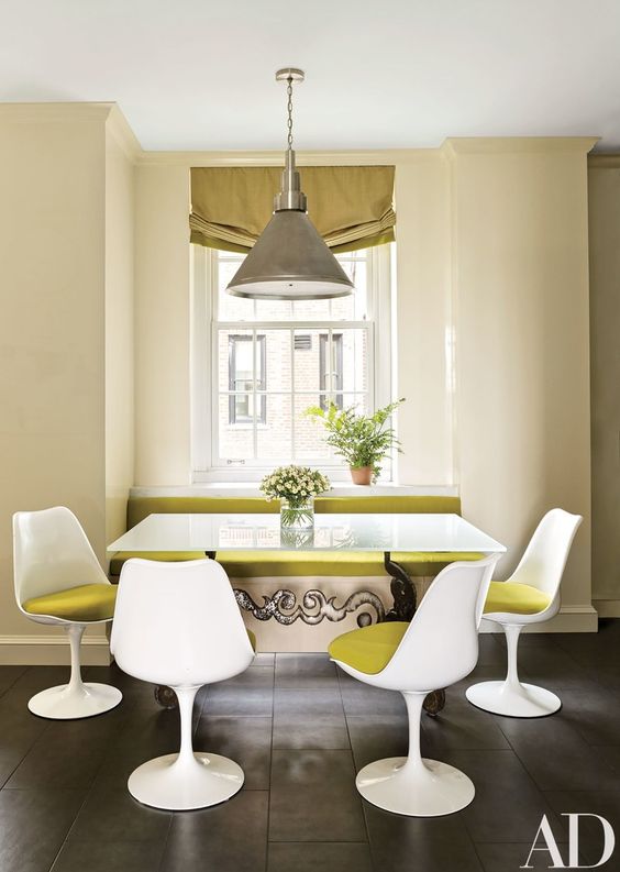 a bold dining space with a windowsill bench with mustard upholstery, a table, and mustard Tulip chairs, a pendant lamp