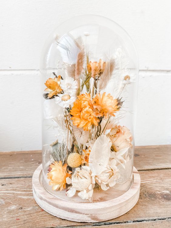 a bold dried flower arrangement in a cloche, with orange and neutral dried blooms, herbs and a bit of greenery is a cool centerpiece