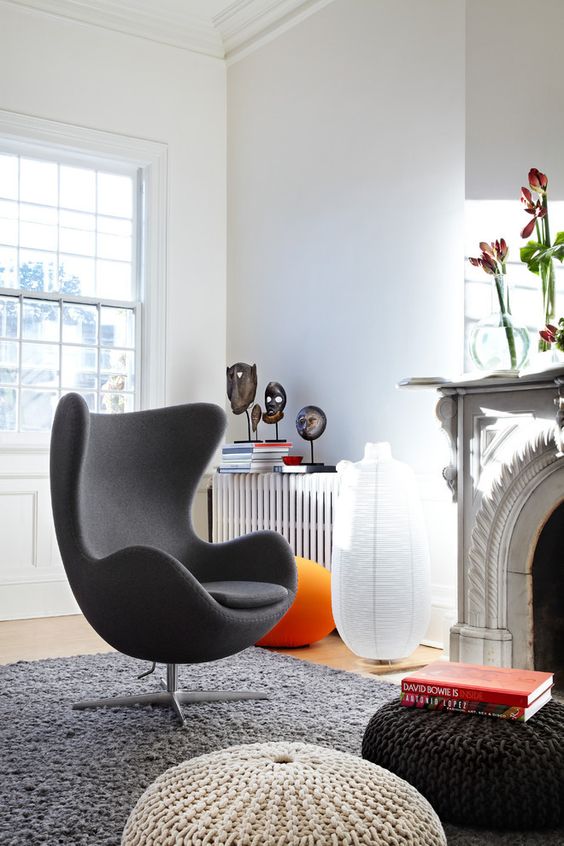 a bold living room with a fireplace and blooms on it, with a grey Egg chair, several knit Poufs and some decor on the radiator