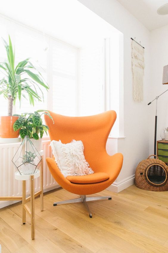 a bold nook with an orange Egg chair, a plant stand and a terrarium, a woven cat house and macrame