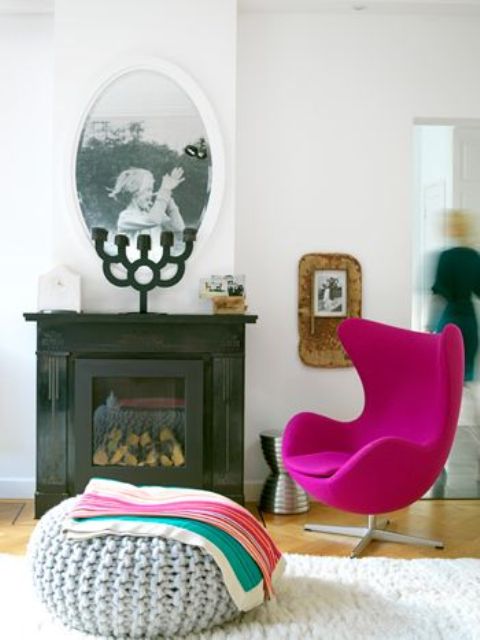 a bold space with a built-in fireplace, a fuchsia Egg chair, a knit pouf, some blankets and decor is a cool nook