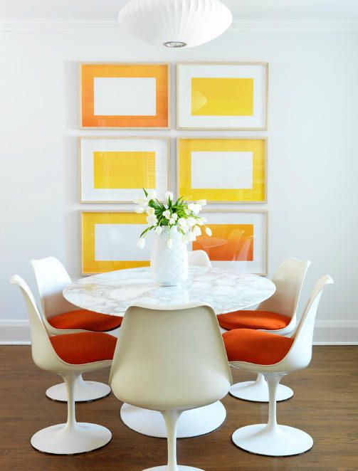 a bright dining space with a colorful gallery wall, a marble top table, orange Tulip chairs and a pendant lamp is super cool