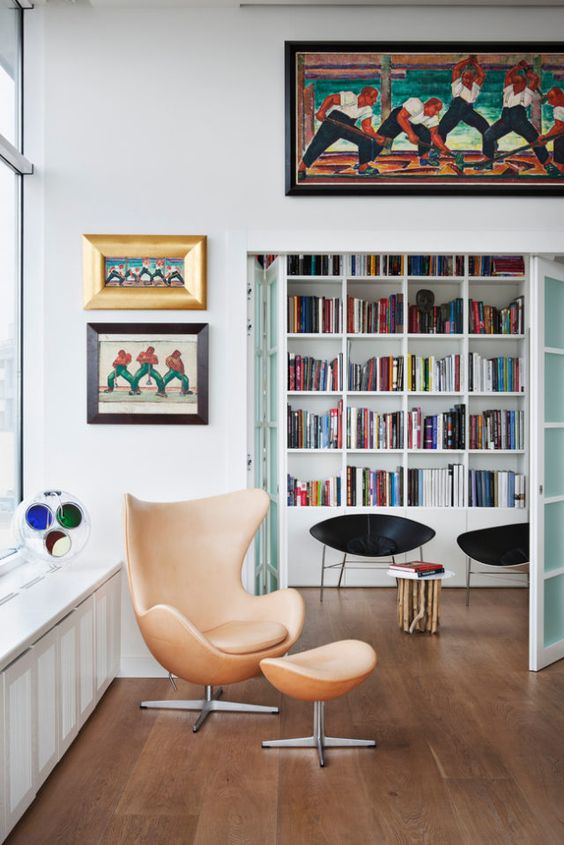 a catchy and bright space with a tan leather Egg chair and a footrest, bold artwork and some black chairs