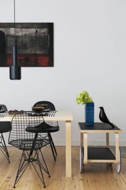 a catchy dining room with a stained table and black Eames wire chairs, a trolley with some decor and black pendant lamps