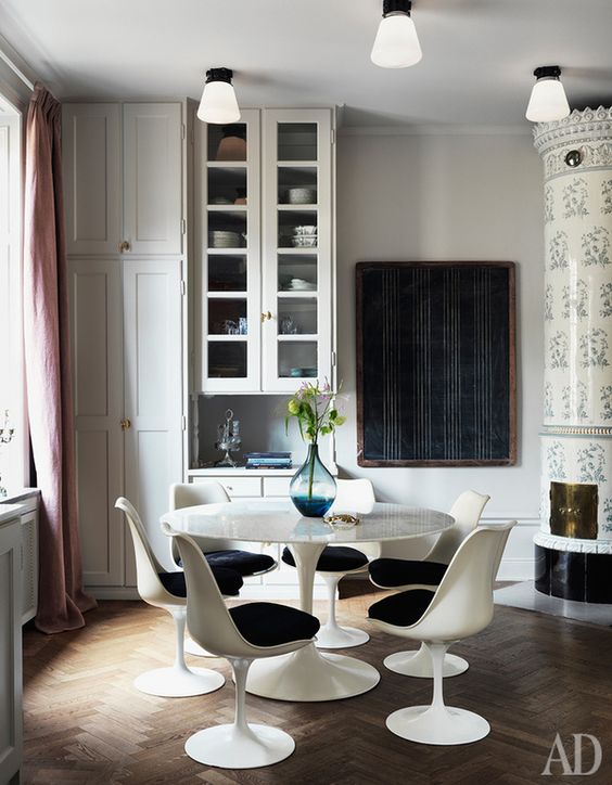 a catchy dining room with several cabinets for storage, a vintage hearth, a round table, black Tulip chairs and pink curtains