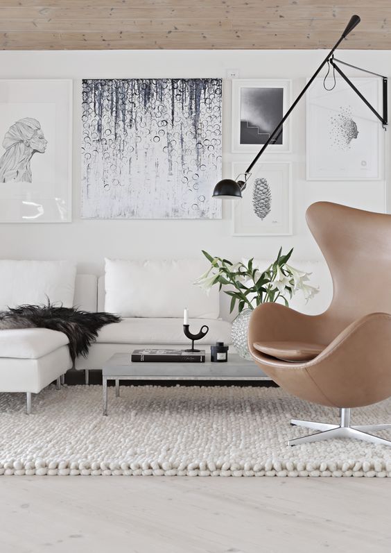 a catchy living room with a creamy corner sofa and pillows, a low coffee table, a gallery wlal and a beige leather Egg chair