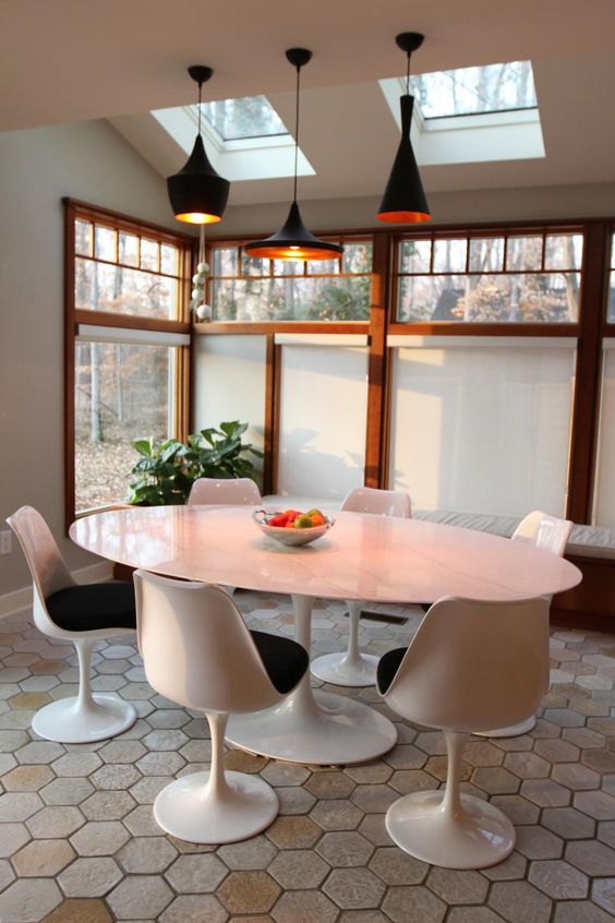 a catchy sunroom with skylights and large windows, an oval table, black Tulip chairs, black pendant lamps and a potted plant