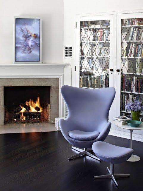 a chic space with a built-in bookcase, a fireplace, a periwinkle Egg chair with a footrest, a side table and an artwork