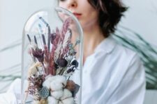 a cloche with a black base, cotton, neutral and pink grasses, bold dried blooms and lotus slices is a cool and bold decoration