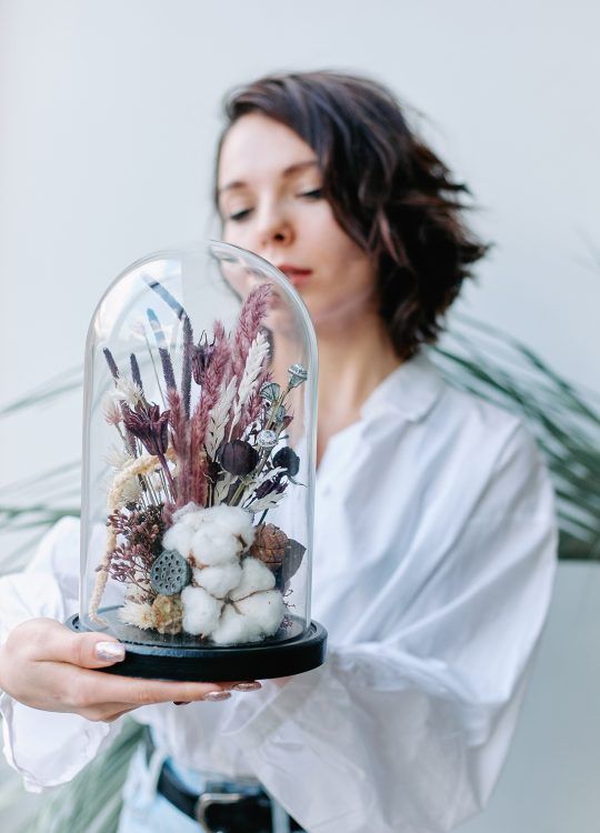 a cloche with a black base, cotton, neutral and pink grasses, bold dried blooms and lotus slices is a cool and bold decoration