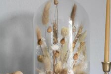 a cloche with a simple dried grass arrangement and seed pods is a cool boho or rustic decor idea that will soften any home decor