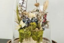 a cloche with a wooden base, moss, dried white, blue and tan blooms, willow, greenery and berries is cool for spring or summer