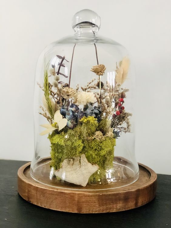 a cloche with a wooden base, moss, dried white, blue and tan blooms, willow, greenery and berries is cool for spring or summer
