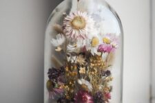 a cloche with a wooden base, with dried white, pink and purple blooms and yellow ones is a lovely summer home decor idea