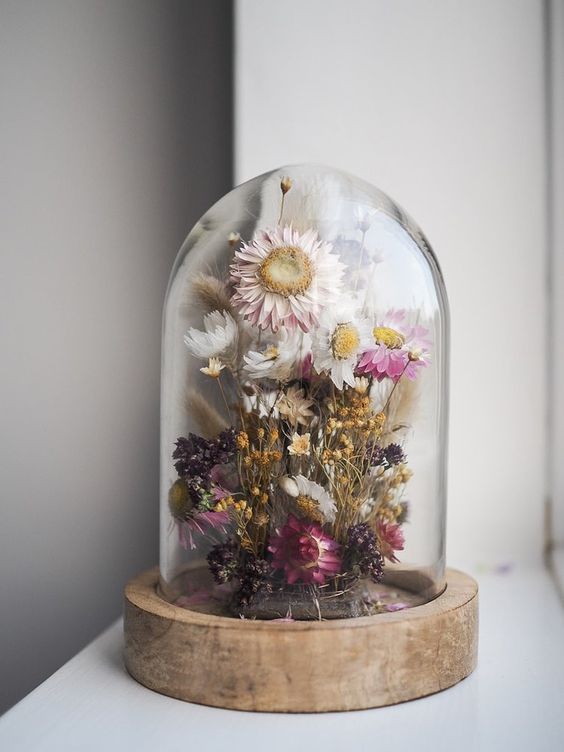 a cloche with a wooden base, with dried white, pink and purple blooms and yellow ones is a lovely summer home decor idea