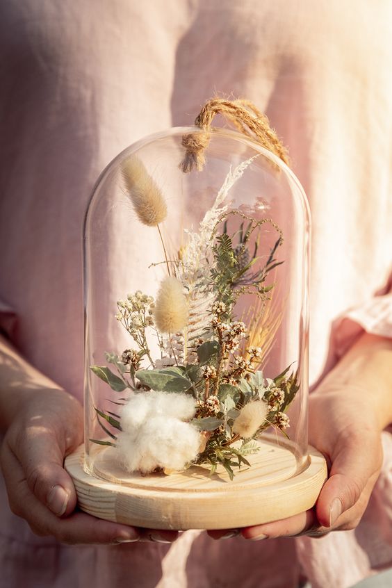 a cloche with a wooden tray, cotton, greenery, grasses and some neutral blooms and thistles is a great decoration for summer
