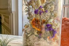a cloche with a wooden tray, moss, dried neutral, purple and rust blooms and some lavender and allium