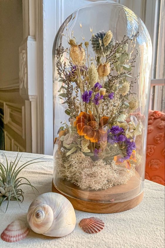 a cloche with a wooden tray, moss, dried neutral, purple and rust blooms and some lavender and allium