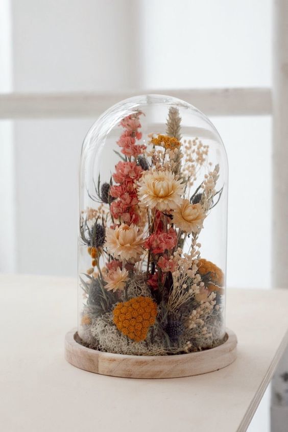 a cloche with dried flowers in pink, orange and rust, with thistles and grasses and moss is a very eye catchy idea