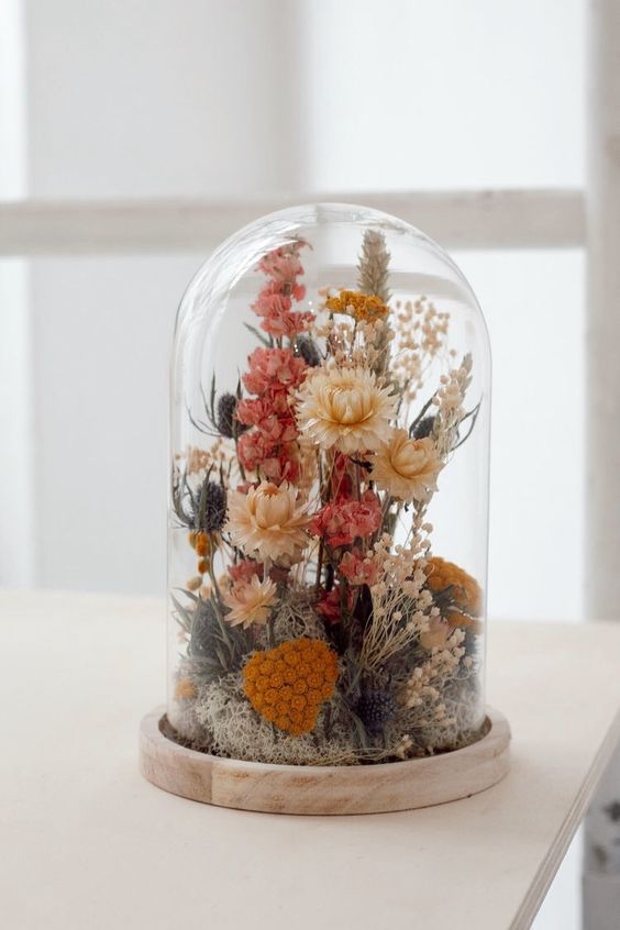 a cloche with dried flowers in pink, orange and rust, with thistles and grasses and moss is a very eye-catchy idea