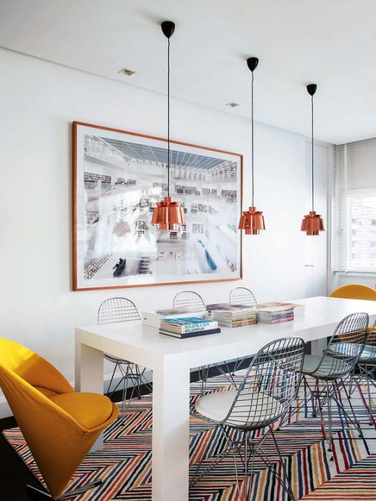 a colorful dining room with a white table, Eames wire chairs, orange pendant lamps, an artwork and marigold chairs
