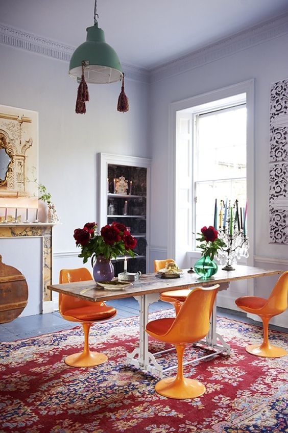 a colorful dining room with lilac walls and a ceiling, a fireplace, a built-in storage unit, a table, orange Tulip chairs, a green pendant lamp