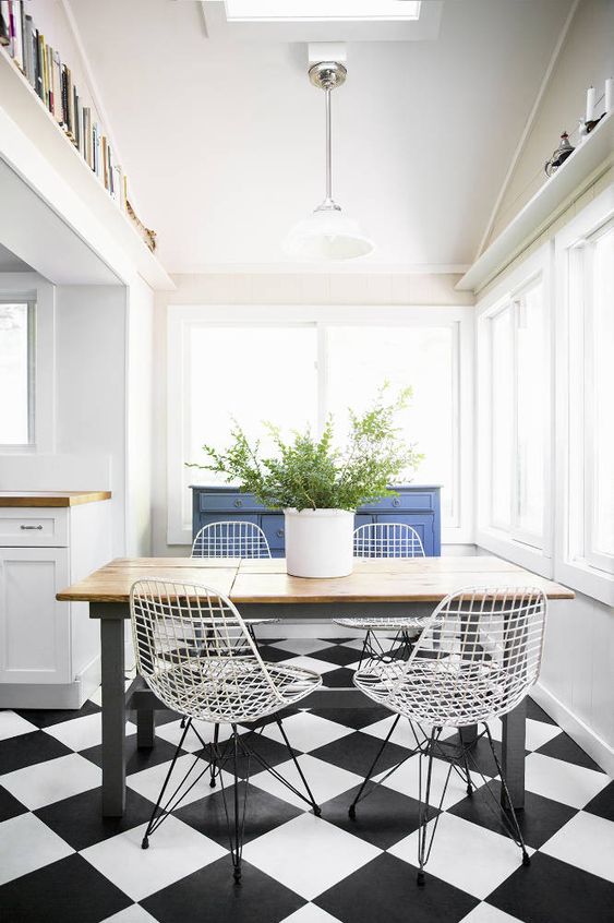 a contrasting dining space by the window, with a blue sideboard, a rustic table, white Eames wire chairs and some greenery