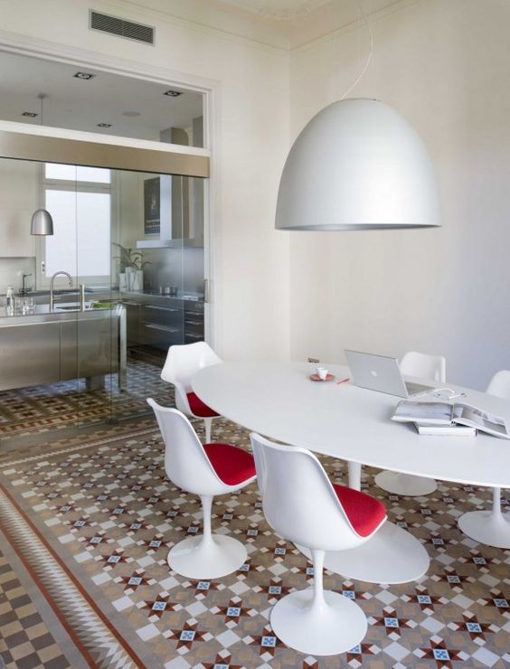 a cool dining and working space with a bold floor, an oval table, red Tulip chairs and a pendant lamp