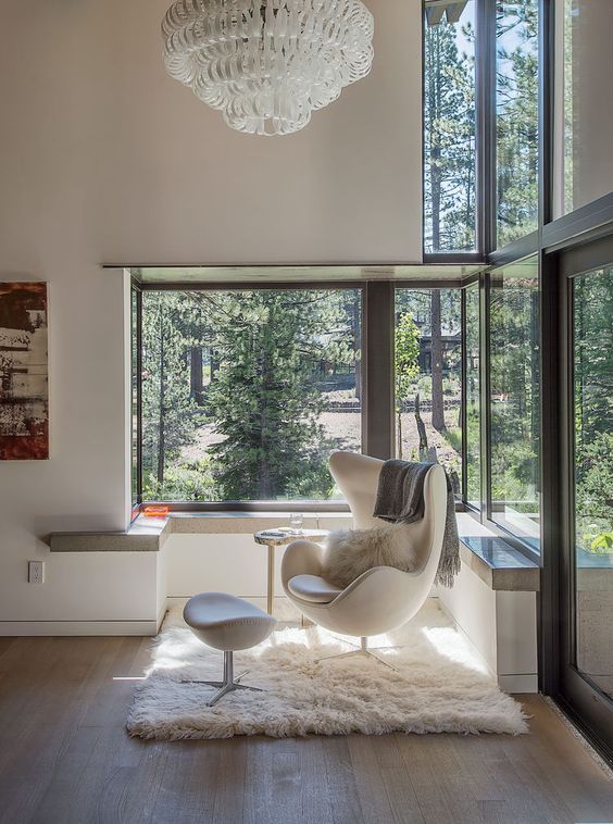 a cool glazed space to enjoy the sun, with a creamy Egg chair and a footrest, a windowsill and a large chandelier