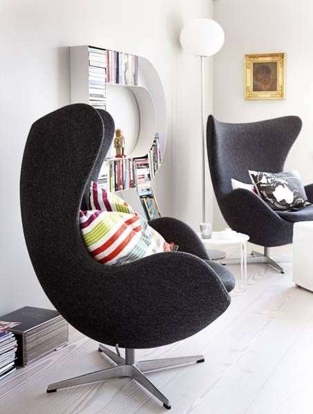 a cool nook with a letter bookshelf, black Egg chairs, colorful pillows, stacks of magazines and a coffee table