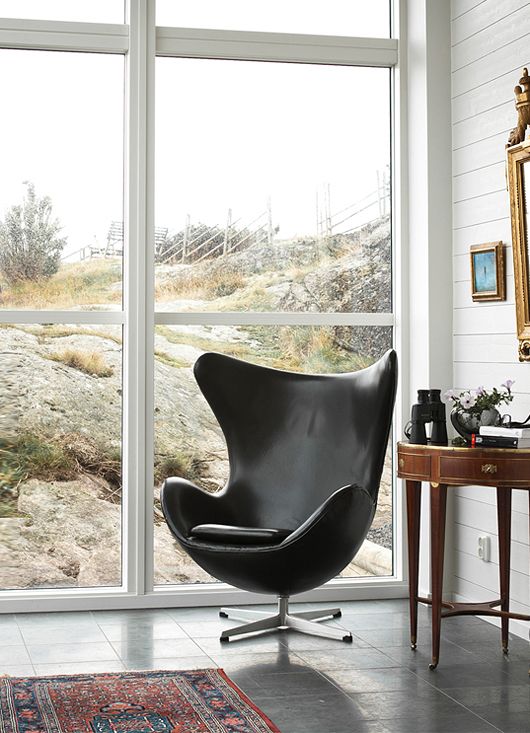 a cool space with a glazed wall, white beadboard walls, a dark-stained side table with decor and a black Egg chair plus some art