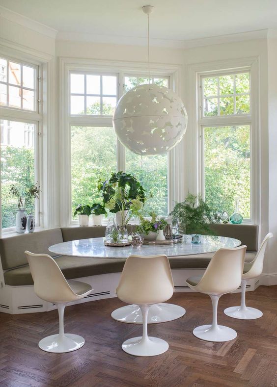 a cozy mid-century modern breakfast nook with a built-in windowsill bench, an oval table, olive green Tulip chairs, a pendant lamp