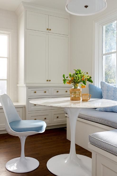a creamy modern farmhouse dining space with storage units, a windowsill bench with pillows, a round table, a blue Tulip chair