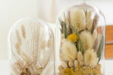 a duo of cloches with dried blooms, grasses, branches and leaves and some berries done in natural colors looks amazing
