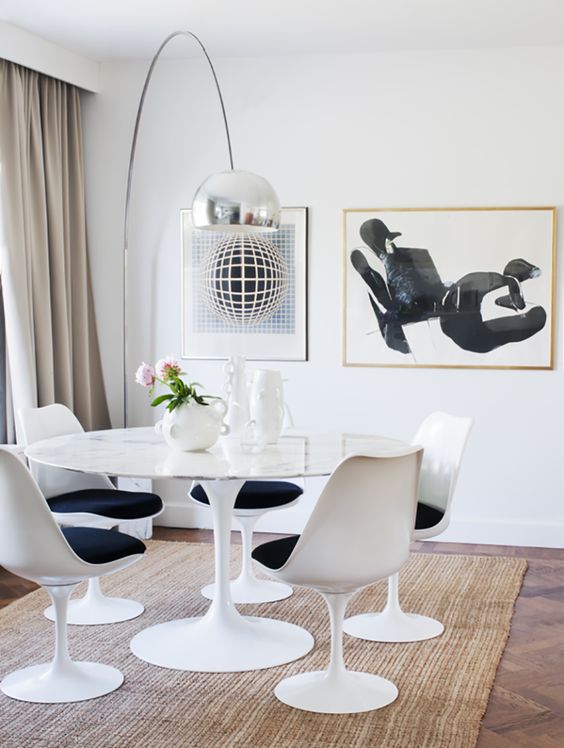 a fab dining space in neutrals with a round table, black Tulip chairs, some artworks, a metallic floor lamp and neutral textiles