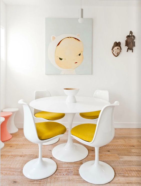 a fun dining space with a round table, mustard Tulip chairs, a fun artwork and Asian decor on the wall, colorful stools