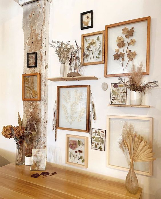 a gallery wall of pressed flowers and leaves in light stained frames and grasses in vases is a cool and chic idea