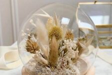 a globe with a wooden base and dried neutral blooms, dried grasses and billy balls plus some leaves is a chic boho decoration