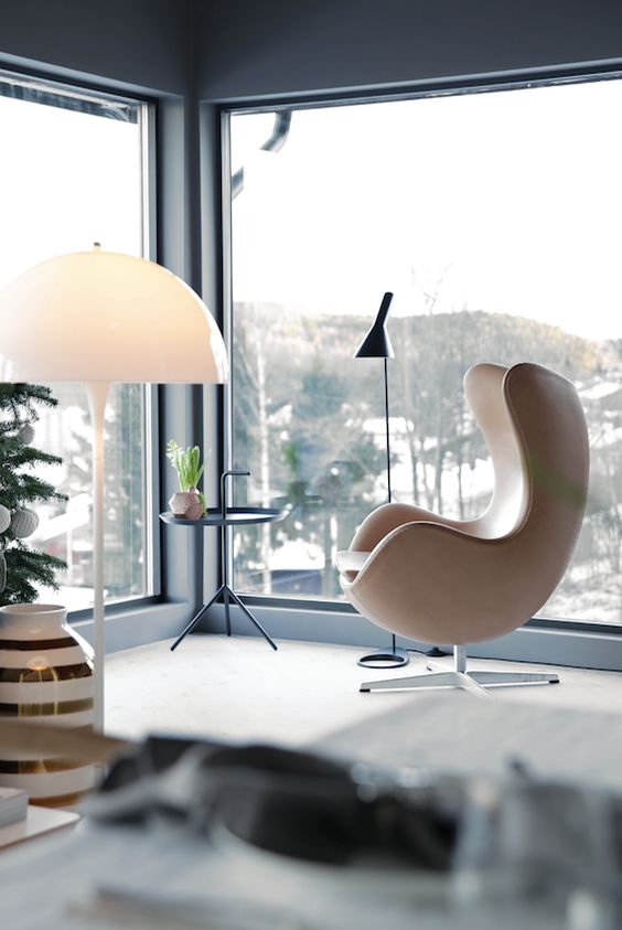 a gorgeous glazed space with a tan leather Egg chair, a side table and a black floor lamp plus some amazing views