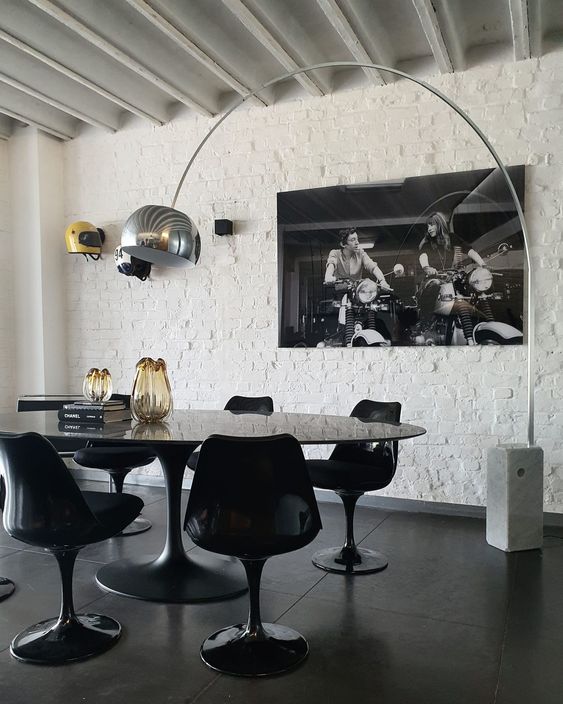 a jaw-dropping dining space with a white brick wall, an oval black table, black Tulip chairs, a floor lamp and a large photo