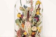 a large cloche with dried bold blooms in purple and burgundy, with billy balls, dried grasses and leaves is a catchy idea for a summer space