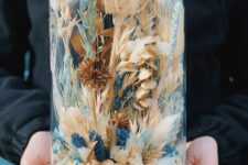 a large cloche with dried white, rust and blue blooms and grasses looks wild and cool and fits a summer or spring space