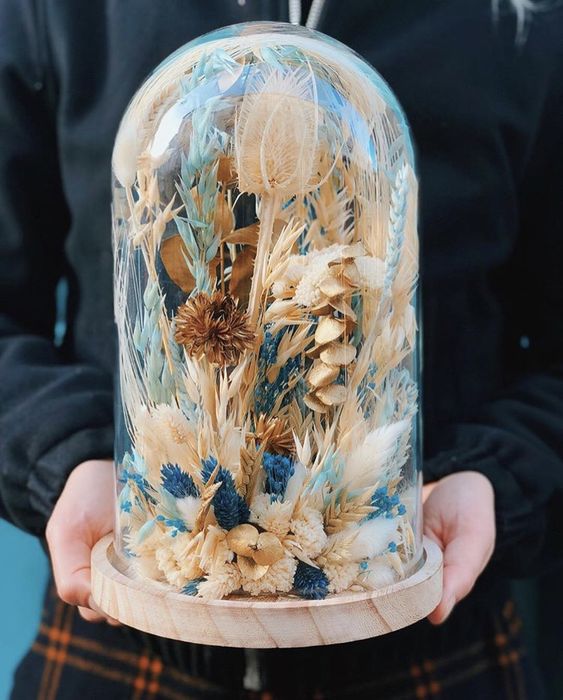 a large cloche with dried white, rust and blue blooms and grasses looks wild and cool and fits a summer or spring space