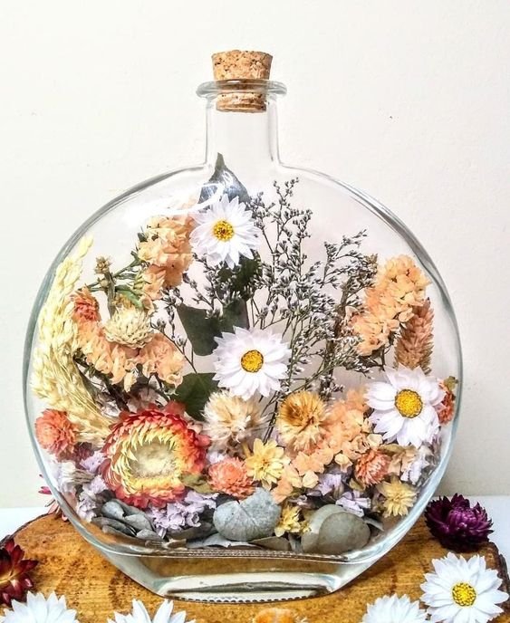 a large flat bottle filled with dried blooms of red, peachy pink and white color, with greenery and some grasses is a lovely summer decoration